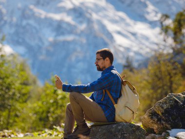 Irkis Vadisi 'nden, Arkhyz' den, Karachay-Cherkessia 'dan, Kuzey Kafkasya' dan. Mavi gökyüzü, bulutlar ve Kafkasya nehri yakınlarındaki güzel ormanla karlı dağ vadisinde yürüyüş yapan bir adam..