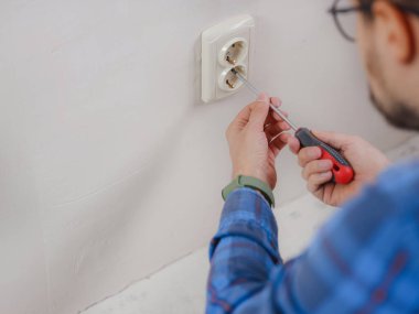 Mavi takım elbiseli genç adam apartman dairesinde çalışıyor. Ev yenileme konsepti. Elektrik soketi kuran elektrikçi