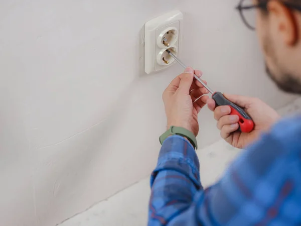stock image young man in blue work suit doing Repair apartment. Home renovation concept. electrician installing power socket