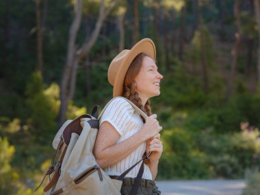 Beyaz, kızıl, genç, güzel, sırt çantalı, ormanda tek başına seyahat eden bir kadın. Çekici gezgin, tatil gezisi sırasında doğa ormanında mutluluk ve eğlenceyle yürürken etrafına bakar ve keşfederdi..