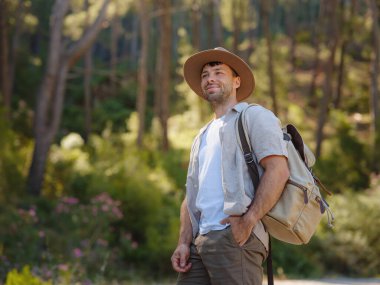 Temiz havayı kucaklama ve açık hava aktiviteleriyle meşgul olma kavramı. Sırt çantalı ve şapkalı bir gezgin dağ ormanında yürüyüş yapıyor. Seyahat Yaz Yaşam Tarzı Konsepti.