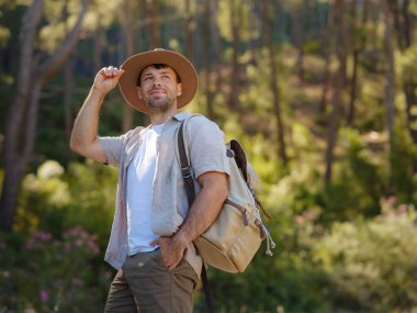 Temiz havayı kucaklama ve açık hava aktiviteleriyle meşgul olma kavramı. Sırt çantalı ve şapkalı bir gezgin dağ ormanında yürüyüş yapıyor. Seyahat Yaz Yaşam Tarzı Konsepti.
