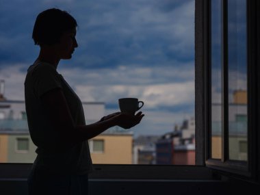 silhouette of a woman with a mug of tea on the background of the city.