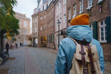 winter travel to Dusseldorf, Germany. young Asian tourist in blue jacket and yellow hat symbol of Ukraine walks through sights of old town or Altstadt. Popular center of Rheinland and Westphalia