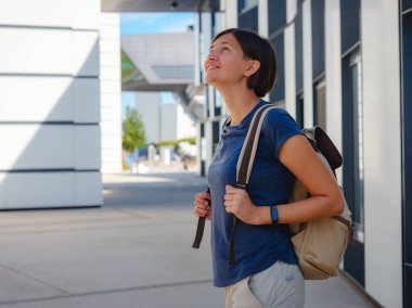 Cheerful asian female student standing outdoors, happy young eastern woman walking in campus Vienna University of Economics, Looking away and smiling, copy Space