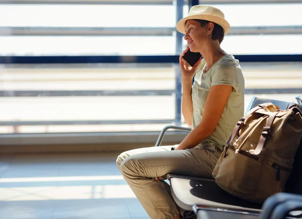 young asian female traveler with hipster backpack and hat at airport waiting for departure at Vienna Airport. Traveling woman Remote Work Online on Mobile Phone in Boarding Lounge of Airline Hub