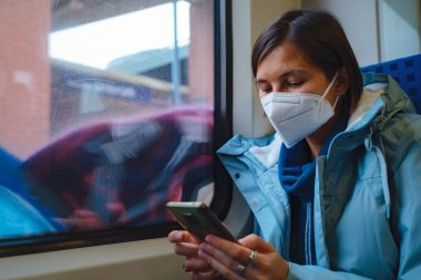 Asian Woman in blue jacket and protective mask use app on smartphone in empty train in winter day. Lifestyle concept.