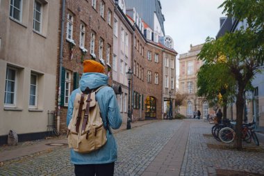 winter travel to Dusseldorf, Germany. young Asian tourist in blue jacket and yellow hat symbol of Ukraine walks through sights of old town or Altstadt. Popular center of Rheinland and Westphalia