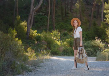 Beyaz, kızıl, genç, güzel, sırt çantalı, ormanda tek başına seyahat eden bir kadın. Çekici gezgin, tatil gezisi sırasında doğa ormanında mutluluk ve eğlenceyle yürürken etrafına bakar ve keşfederdi..