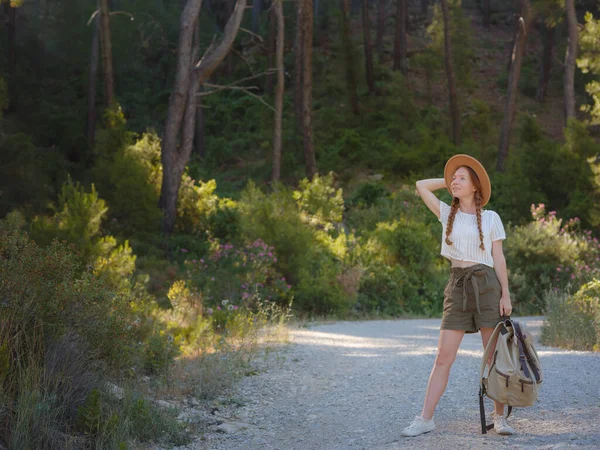 Beyaz, kızıl, genç, güzel, sırt çantalı, ormanda tek başına seyahat eden bir kadın. Çekici gezgin, tatil gezisi sırasında doğa ormanında mutluluk ve eğlenceyle yürürken etrafına bakar ve keşfederdi..