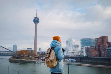 autumn or winter travel to Dusseldorf, Germany. young Asian tourist or student in blue jacket and yellow hat  symbol of Ukraine walks through sights of European city. beautiful view in the Media Bay