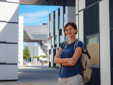 Cheerful asian female student standing outdoors, happy young eastern woman walking in campus Vienna University of Economics, Looking away and smiling, copy Space