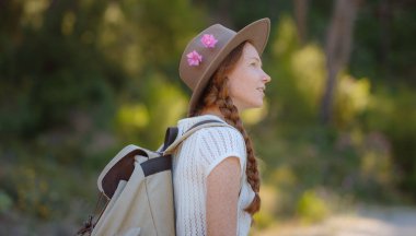 Beyaz, kızıl, genç, güzel, sırt çantalı, ormanda tek başına seyahat eden bir kadın. Çekici gezgin, tatil gezisi sırasında doğa ormanında mutluluk ve eğlenceyle yürürken etrafına bakar ve keşfederdi..