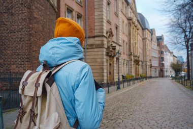 winter travel to Dusseldorf, Germany. young Asian tourist in blue jacket and yellow hat (symbol of Ukraine) walks through sights of old town or Altstadt. Popular center of Rheinland and Westphalia