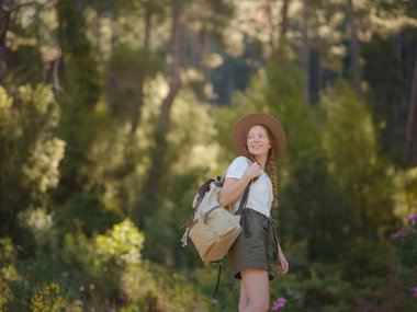 Beyaz, kızıl, genç, güzel, sırt çantalı, ormanda tek başına seyahat eden bir kadın. Çekici gezgin, tatil gezisi sırasında doğa ormanında mutluluk ve eğlenceyle yürürken etrafına bakar ve keşfederdi..