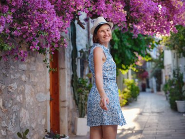 Çiçekli begonviller, eski Bodrum kasabasının sokakları, Türkiye. Romantik caddelerde yürüyen beyaz şık elbiseli mutlu bir gezgin kadın. Yaz gezisi