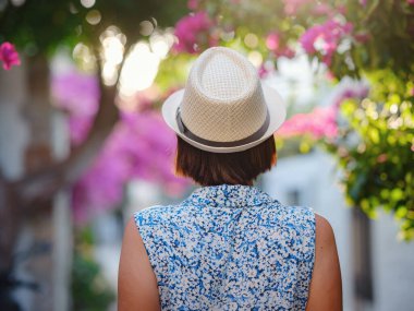 Blooming bougainvillea, streets of the old town of Bodrum, Turkey. Happy traveler woman in white elegant outfit walking by romantic streets . Summer travelling