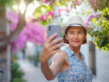 Blooming bougainvillea, streets of the old town of Bodrum, Turkey. Happy traveler woman in white elegant outfit walking by romantic streets . Summer travelling