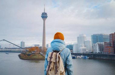 autumn or winter travel to Dusseldorf, Germany. young Asian tourist or student in blue jacket and yellow hat  symbol of Ukraine walks through sights of European city. beautiful view in the Media Bay