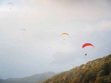 Gökyüzünde paraşütle atlıyor. Bulutlu bir günde denizin ve dağların üzerinde uçan paraglider ikilisi. Türkiye 'nin Oludeniz kentindeki Paraşütçü ve Mavi Göl manzarası. Olağanüstü bir spor. Peyzaj