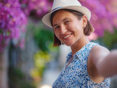 Blooming bougainvillea, streets of the old town of Bodrum, Turkey. Happy traveler woman in white elegant outfit walking by romantic streets . Summer travelling