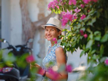 Blooming bougainvillea, streets of the old town of Bodrum, Turkey. Happy traveler woman in white elegant outfit walking by romantic streets . Summer travelling