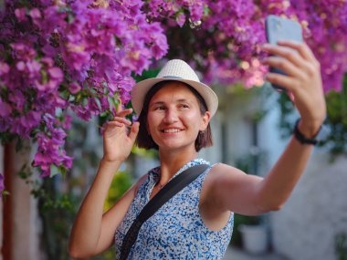 Çiçekli begonviller, eski Bodrum kasabasının sokakları, Türkiye. Romantik caddelerde yürüyen beyaz şık elbiseli mutlu bir gezgin kadın. Yaz gezisi