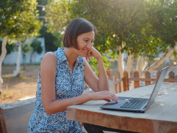 Happy young asian woman with laptop resting outdoors in tiny house in summer garden, weekend away and remote office idea, early morning. Tiny houses and Small Living concept.