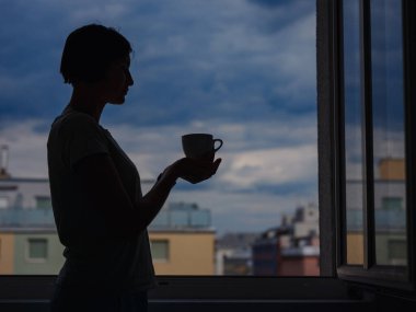 silhouette of a woman with a mug of tea on the background of the city.