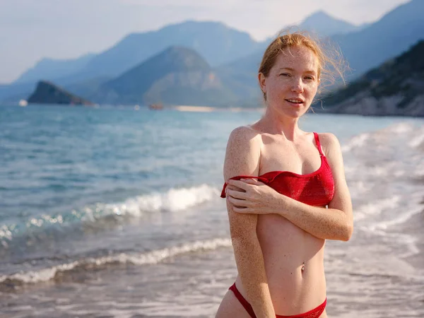 stock image Beautiful ginger woman in red bikini on tropical beach. Portrait of happy young lady smiling at sea. Happy girl with red hair and freckles enjoying the sun. concept of safe interaction with sun