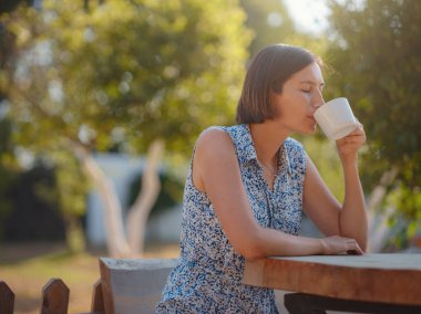 Kadın kahve içiyor, sabah rutini küçük evinin yanında. İlk mülk. Yaz bahçesinde küçük bir daire. Minimalizm. İçeri giriyoruz. Yalnız yaşamak. Büyüleyici karavan evi.