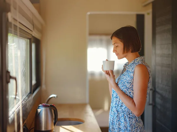 Young woman enjoying cup of coffee at morning, in her kitchen. Minimalism. Moving in. Living alone. Charming trailer house