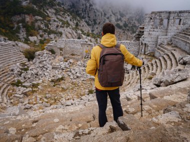 Sonbahar yürüyüşü, sarı ceketli adam Termessos Antik Kenti, Türkiye 'deki antik amfitiyatroya bakıyor. Türkiye 'nin en seçkin arkeolojik sahaları ve başlıca turizm merkezlerinden biri.