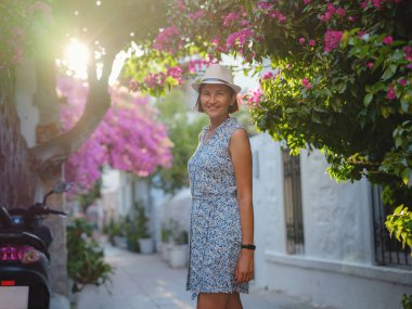 Çiçekli begonviller, eski Bodrum kasabasının sokakları, Türkiye. Romantik caddelerde yürüyen beyaz şık elbiseli mutlu bir gezgin kadın. Yaz gezisi