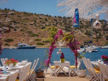 Bodrum 'dan Türkiye' ye yaz yolculuğu. Bodrum, Gumusluk Town 'daki Ege balık lokantası masası. Restoran masaları ve sandalyeler denizde.