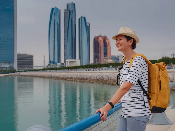 アラブ首長国連邦への旅行 ダウンタウンアブダビの街並みへのバックパックと帽子の景色を持つ幸せな若いアジアの女性旅行者 休暇と観光地のコンセプト — ストック写真