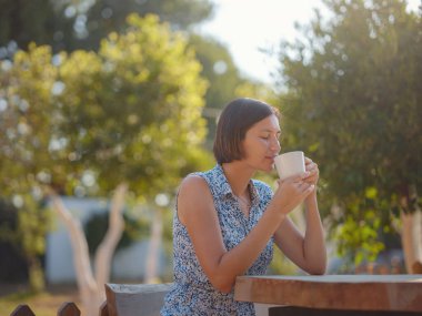 Kadın kahve içiyor, sabah rutini küçük evinin yanında. İlk mülk. Yaz bahçesinde küçük bir daire. Minimalizm. İçeri giriyoruz. Yalnız yaşamak. Büyüleyici karavan evi.