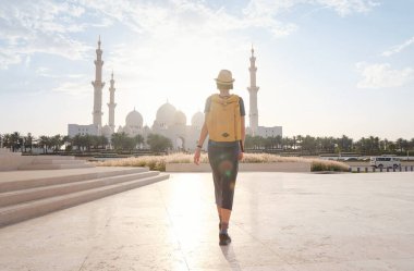 Birleşik Arap Emirlikleri 'ne seyahat, Wahat Al Karama ya da Haysiyet Vahası' nda sırt çantası ve şapkası olan mutlu Asyalı genç bayan gezgin şehitleri için kalıcı anıt ve Shaikh Zayed Büyük Camii..