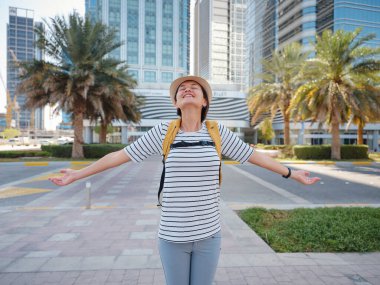 Birleşik Arap Emirlikleri 'ne seyahat, büyük Abu Dabi şehrinde sırt çantası ve şapkası olan mutlu Asyalı genç bayan gezgin. Tatil ve turizm konsepti.