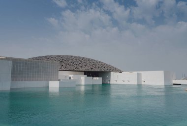 Abu Dabi, BAE - 21 Mart 2023 Louvre Abu Dabi ünlü müzesinin dışı. Zümrüt yeşili hendeği çevreleyen düz beyaz duvarlar süslü bir kubbe çatısı ile kaplı.