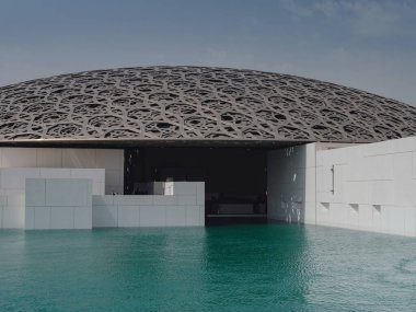 Abu Dabi, BAE - 21 Mart 2023 Louvre Abu Dabi ünlü müzesinin dışı. Zümrüt yeşili hendeği çevreleyen düz beyaz duvarlar süslü bir kubbe çatısı ile kaplı.