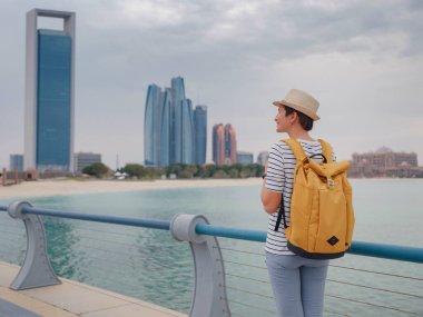 Birleşik Arap Emirlikleri 'ne seyahat sırt çantası ve şapka takıp Abu Dabi şehir merkezine giden mutlu Asyalı genç bayan gezgin. Tatil ve turizm konsepti.