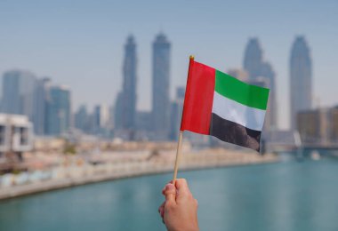 Dubai siluetine karşı BAE 'nin küçük bayrağını tutan bir kadın eli. BAE ulusal kutlama ruhunun fotoğrafı..