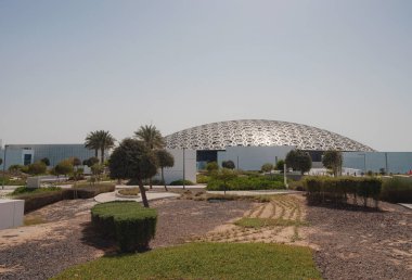 Abu Dabi, BAE - 21 Mart 2023 Louvre Abu Dabi ünlü müzesinin dışı. Zümrüt yeşili hendeği çevreleyen düz beyaz duvarlar süslü bir kubbe çatısı ile kaplı.