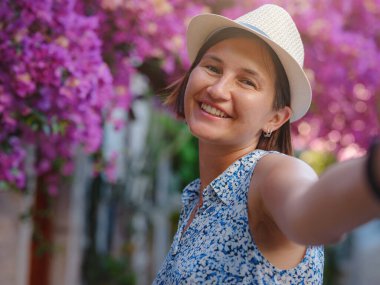 Blooming bougainvillea, streets of the old town of Bodrum, Turkey. Happy traveler woman in white elegant outfit walking by romantic streets . Summer travelling