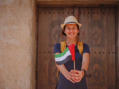 Eski Dubai, BAE 'ye turist gezisi. Al Seef Heritage Souq, Dubai ve Creek 'in eski dar sokaklarında BAE bayrağı taşıyan Asyalı kadın turist. Seyahat ve gezi seyahat konsepti