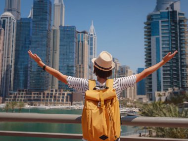 Sarı sırt çantalı çekici Asyalı kadın Dubai Marina bölgesinde gezinti güvertesinde yürüyor. BAE 'de seyahat yerleri ve turist yaşam tarzı