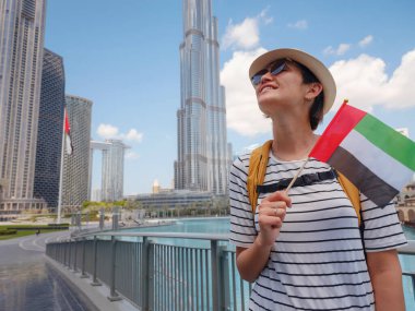 Birleşik Arap Emirlikleri 'nde iyi yolculuklar. Üzerinde Birleşik Arap Emirlikleri bayrağı olan sarı sırt çantalı genç bir kadın güneşli yaz gününde Dubai 'de yürüyor..