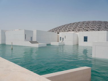 Abu Dabi, BAE - 21 Mart 2023 Louvre Abu Dabi ünlü müzesinin dışı. Zümrüt yeşili hendeği çevreleyen düz beyaz duvarlar süslü bir kubbe çatısı ile kaplı.