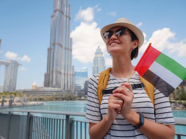 Birleşik Arap Emirlikleri 'nde iyi yolculuklar. Üzerinde Birleşik Arap Emirlikleri bayrağı olan sarı sırt çantalı genç bir kadın güneşli yaz gününde Dubai 'de yürüyor..